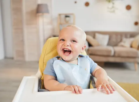 Smiling baby in high chair, supporting baby feeding tips and nutrition advice for first foods